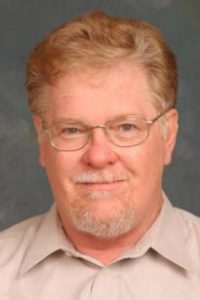 Headshot of Buz McKim showing him with reddish hair, wire glasses, and a goatee.