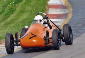 A red Formula Vee drives around a curve on a racetrack.