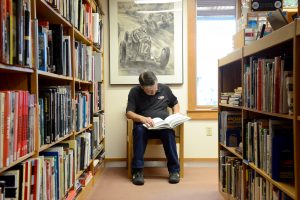 A visitor to the IMRRC sits in a chair and studies a book among the archive's stacks.